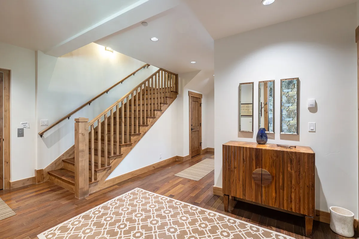 A light-filled entry hall with a staircase, wooden console table, mirrors, and a cozy area rug. The space feels inviting and organized, perfectly suited for welcoming guests and transitioning from outdoors to indoors.