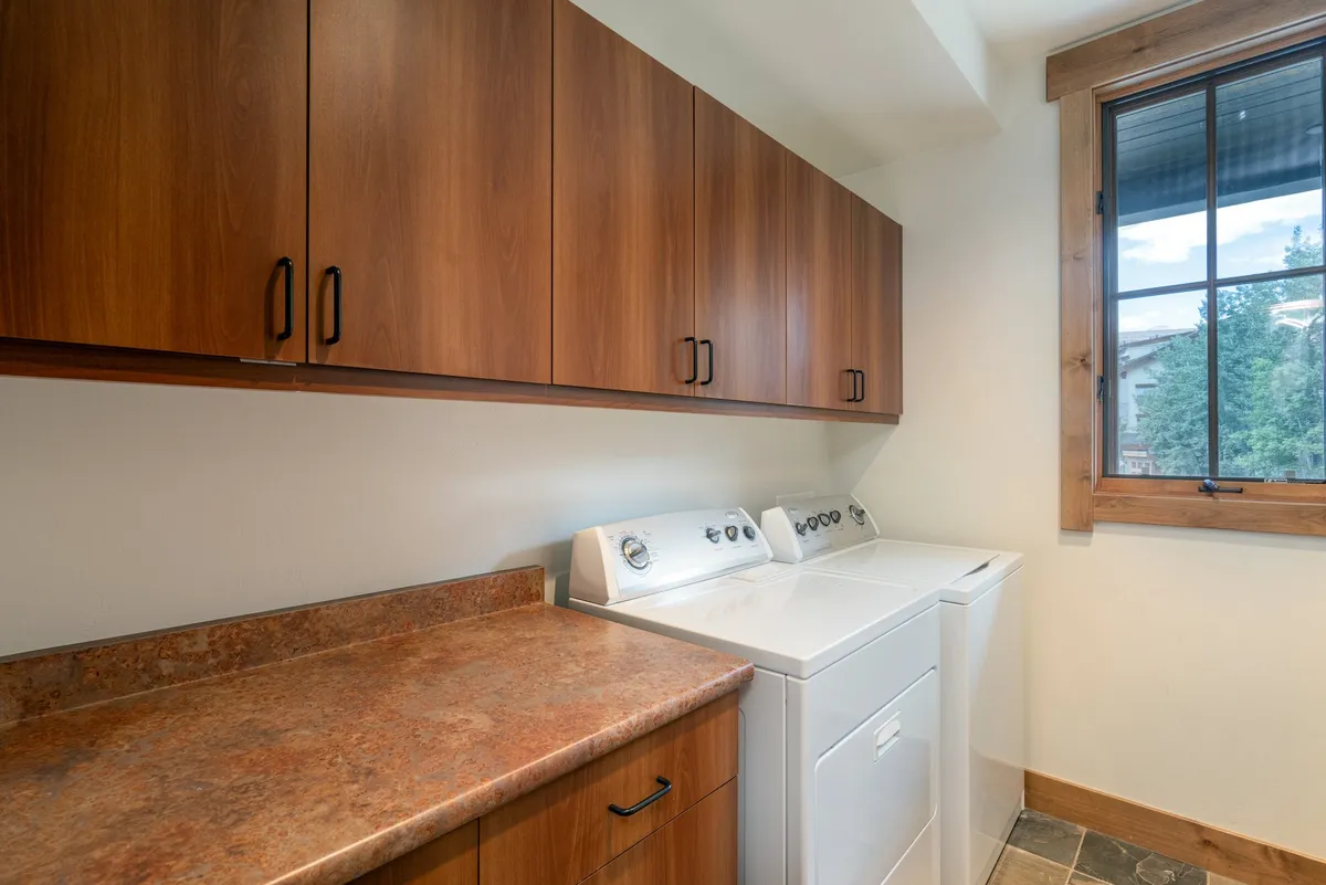 A dedicated laundry room featuring a washing machine, dryer, wooden cabinets, and a countertop for folding clothes. The area is bright and organized, emphasizing practical convenience.