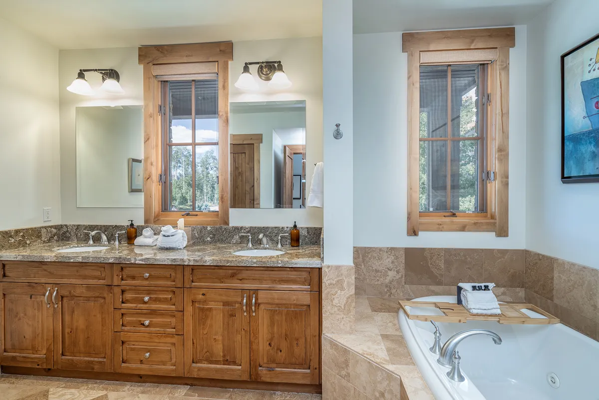 A luxurious bathroom space with double sink vanity, a freestanding bathtub, and large windows pouring in daylight. The decor is elegant and soothing, with wall art and thoughtful details that create a spa-like environment.