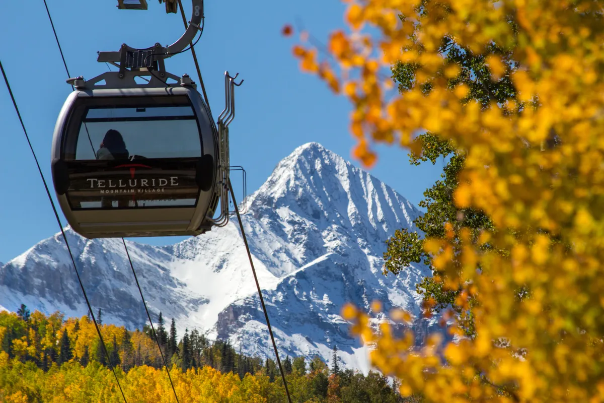 A scenic view featuring a gondola gliding above snow-capped mountains and vibrant autumn foliage. The image evokes adventure and accessibility to outdoor activities, whether for skiing, hiking, or simply enjoying the breathtaking landscape.