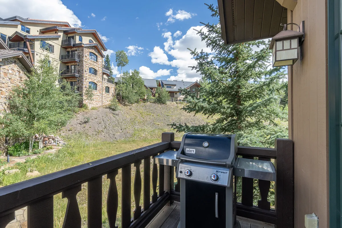 This image shows an outdoor deck with a grill, sturdy railing, and lush greenery all around. The space is set up for barbecuing and casual relaxation, suggesting a morning coffee spot or evening gathering. The deck’s position hints at great views and easy access to nature, connecting the home to its adventurous surroundings.