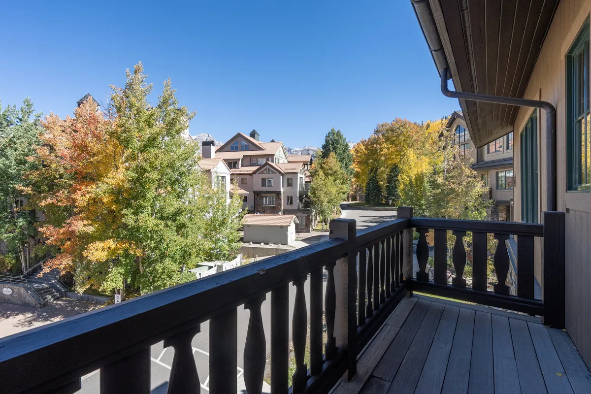 A tranquil balcony scene with a railing overlooking autumn foliage and nearby buildings, inviting relaxation and private enjoyment of the outdoors. The mood is peaceful and contemplative.